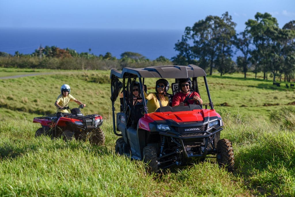 Riders enjoying an ATV adventure at Umauma Experience surrounded by waterfalls and rainforest scenery