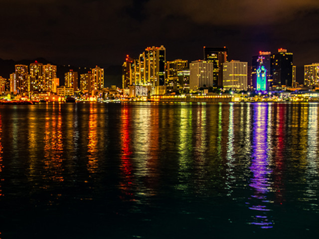 Oahu at night from the ocean with Honolulu city lights reflecting across calm Pacific waters